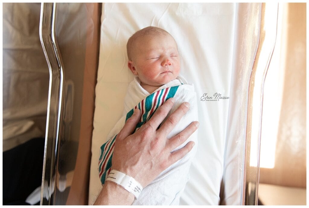 Dad's hand resting on top of newborn baby in hospital bassinette during Grand Rapids fresh 48 photo session