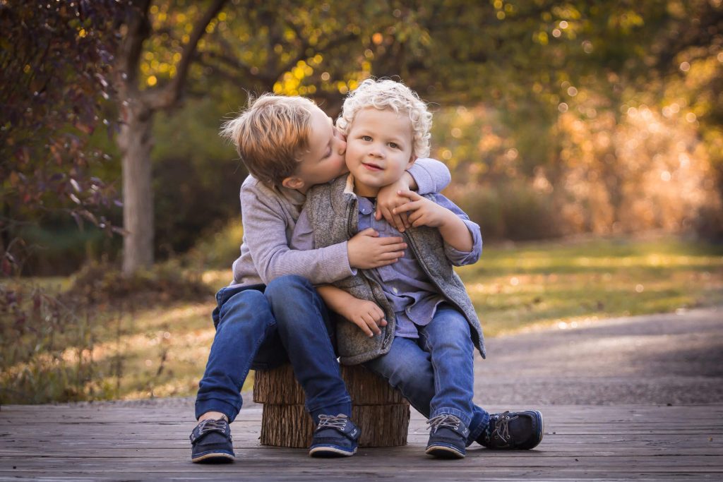 boy kissing younger brother's cheek sitting on tree stumps
