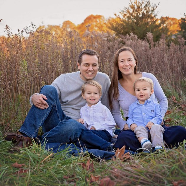 Family of four sitting on a blanket in a tall grass field at sunset