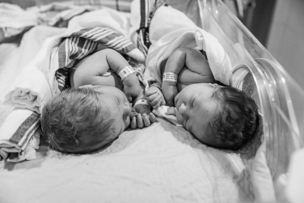 black and white boy and girl twins snuggled in hospital isolette