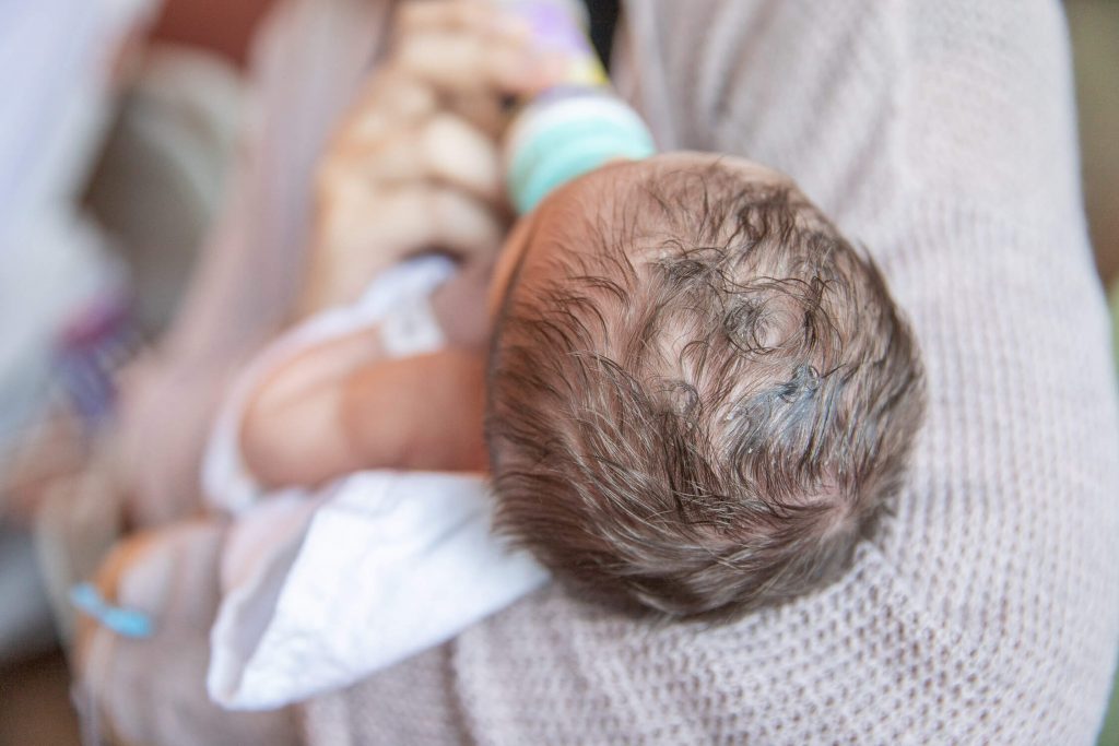 close up of newborn dark hair curls while being bottle fed at hospital