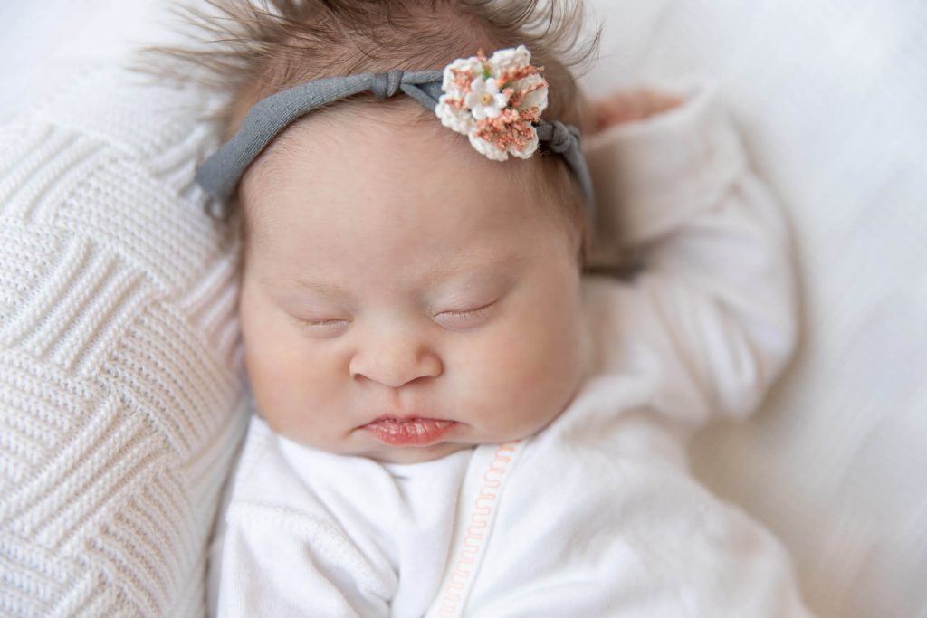 newborn girl wearing gray and pink headband sleeping on white blanket