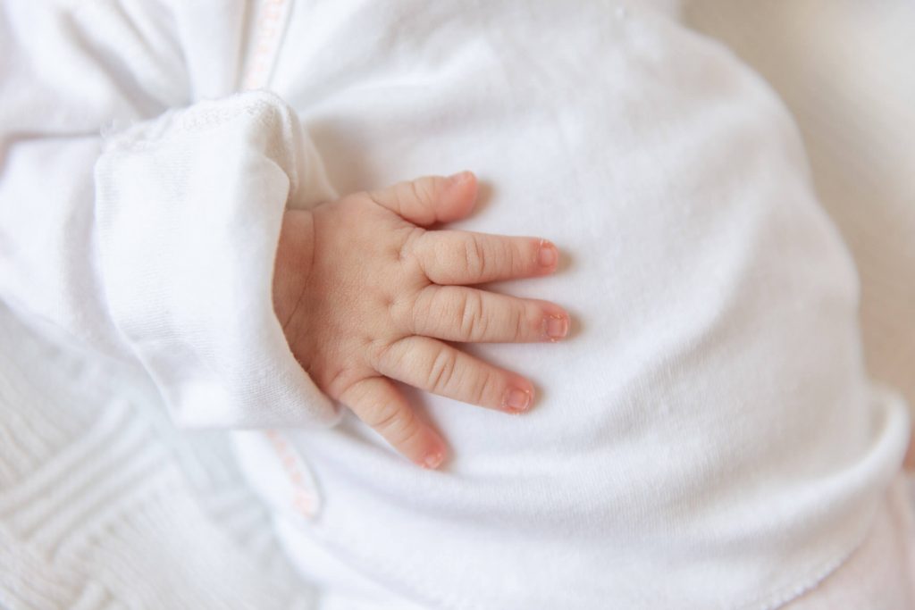 close up of dimpled newborn hand on white onesie
