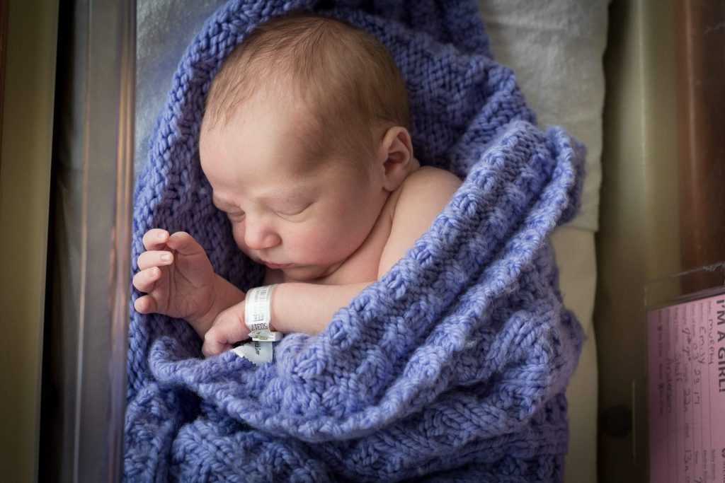 newborn girl wrapped in purple blanket in hospital bassinet