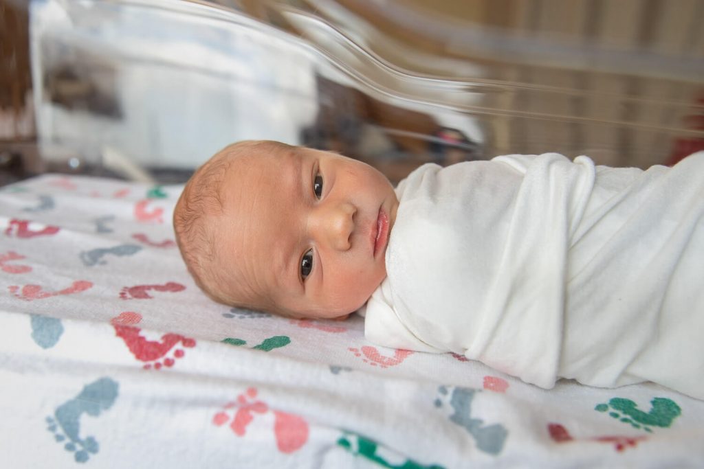 newborn boy staring at camera through hospital bassinet