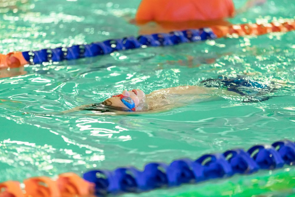 young boy with blue goggles swimming on his back at Goldfish Swim School