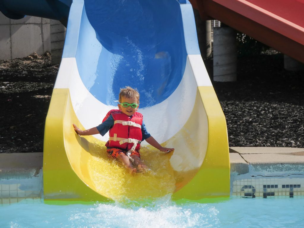 toddler boy wearing a life jacket and goggles sliding down a water slide at Michigan's Adventure