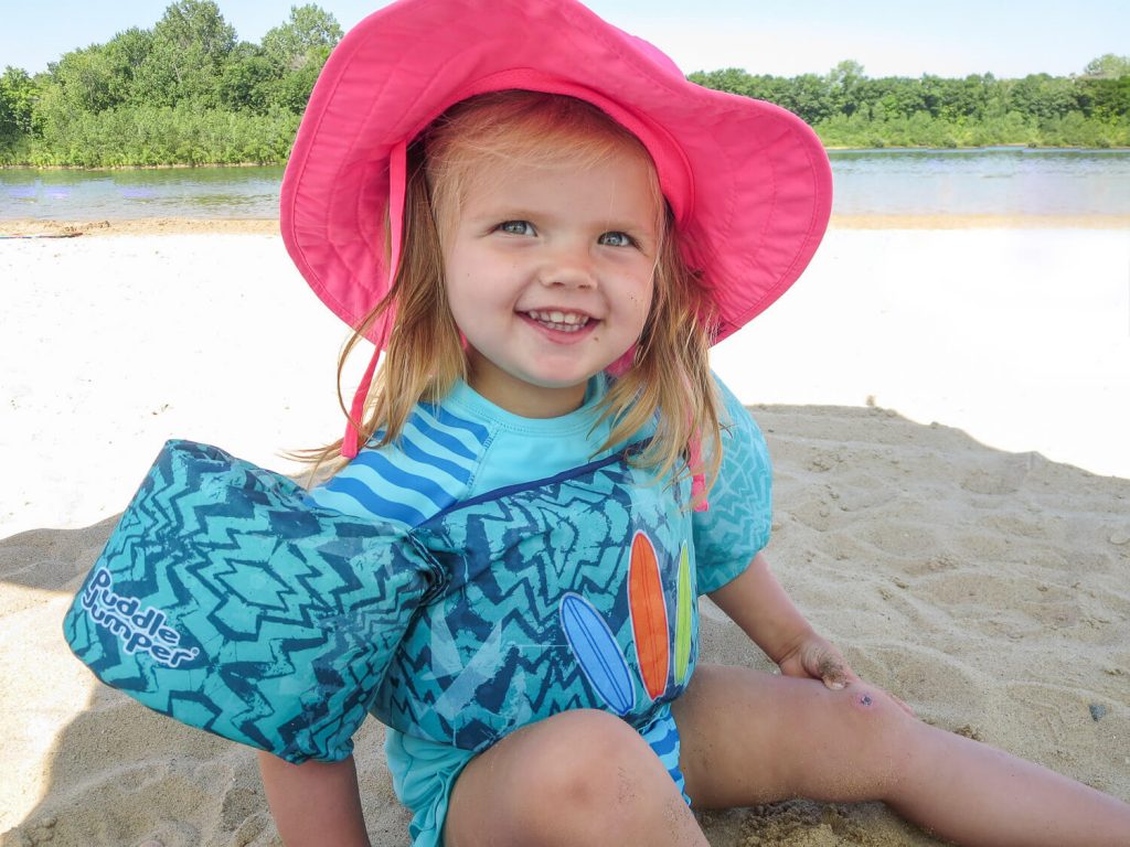 toddler girl wearing a pink sun hat sitting in the sand at Millennium Park in Grand Rapids