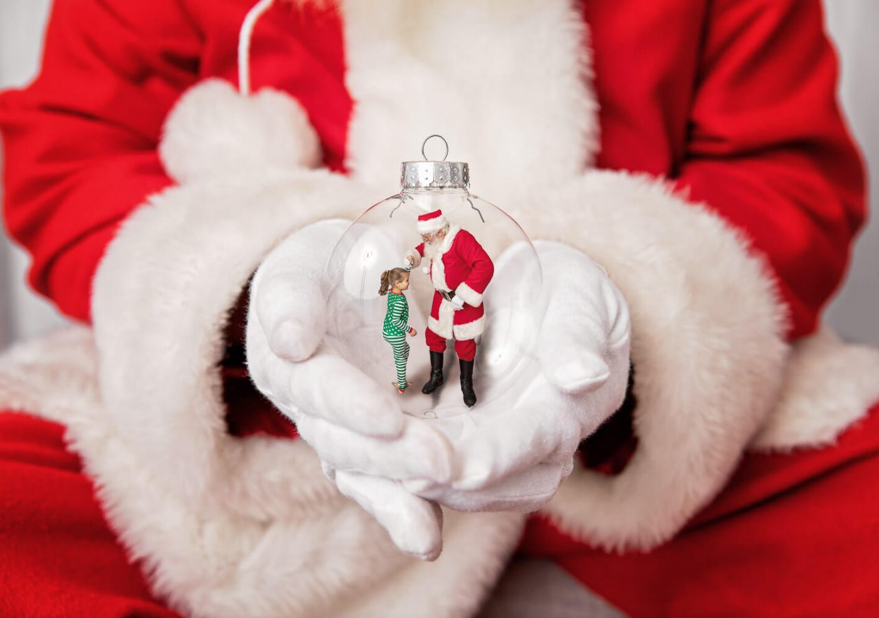 Composite of Santa's hands holding an ornament with a young girl dancing with Santa