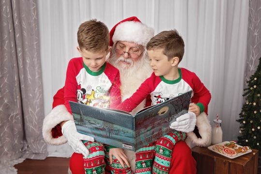 two young boys reading a book on Santa's lap with light coming out of the book