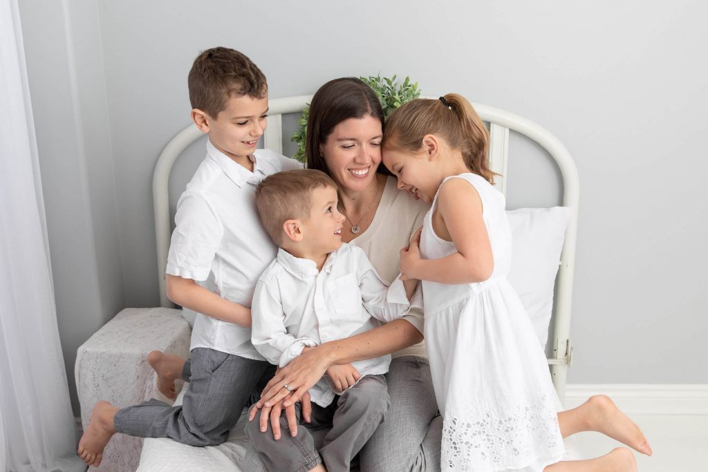 Photographer Erin massie snuggled with her three young children on a bed in a white studio