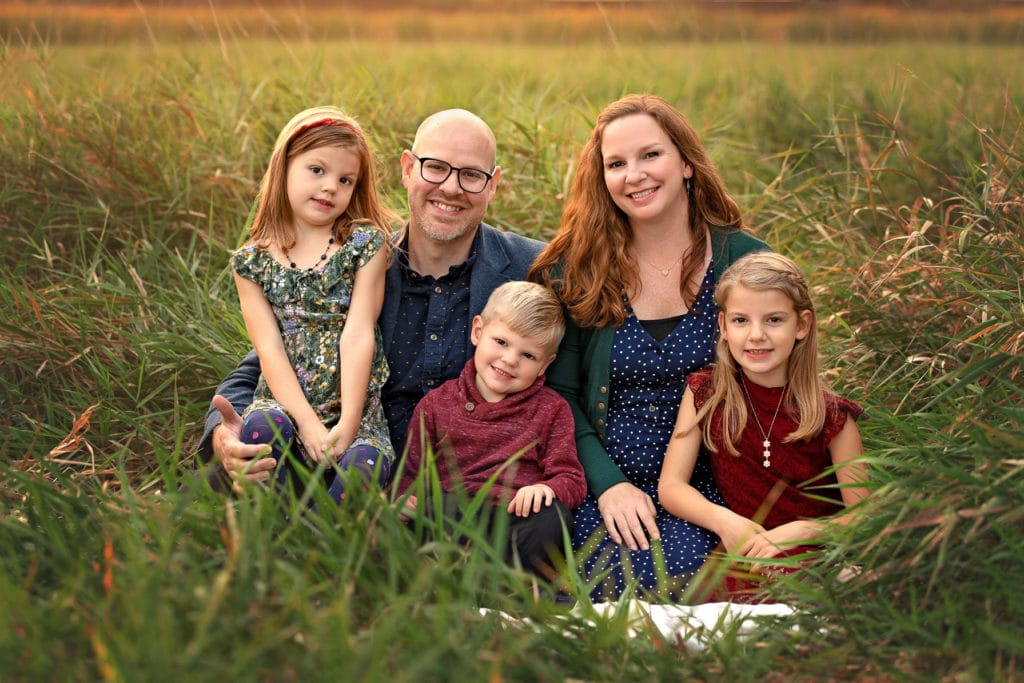 Family of 5 posed sitting together in tall green grasses at sunset in the Fall at Roselle Park
