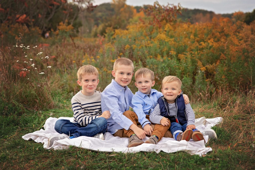 4 young brothers sitting together on a blanket in the middle of a colorful field in Fall at Roselle Park