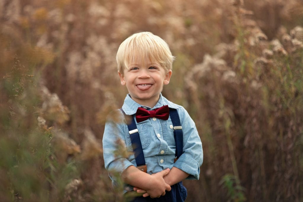Toddler boy sticking his tongue out while grinning surrounded by bronze tall fluffy grasses at Roselle Park