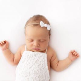 Newborn baby girl laying on a white background wearing a white romper