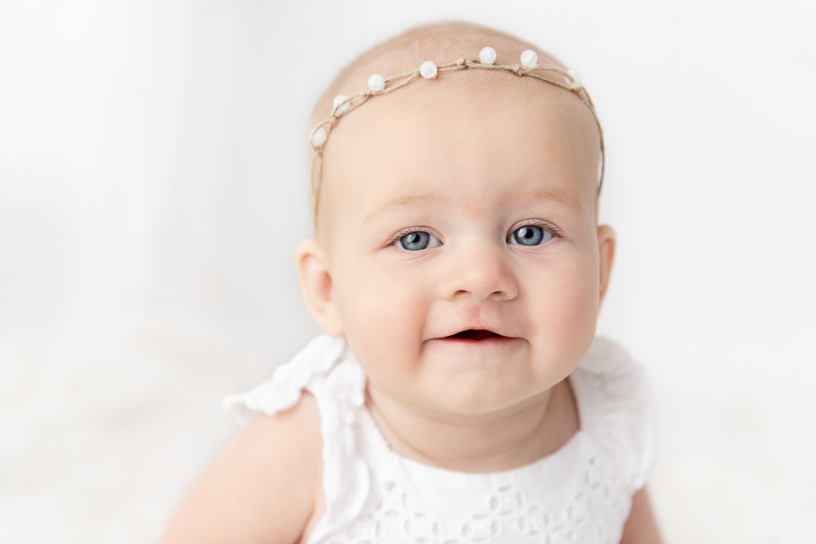 Close up of a 6 month baby girl wearing a white stone headband with big blue eyes