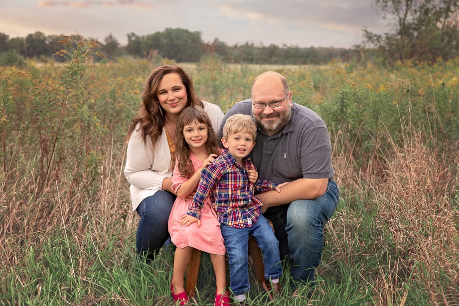 Family of 4 kneeling together in a tall grass field