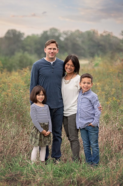 Family of 4 standing together in the middle of a tall grass field