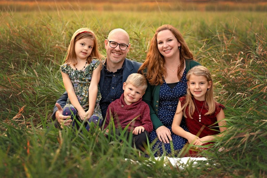 Family of 5 posed sitting together in tall green grasses at sunset in the Fall
