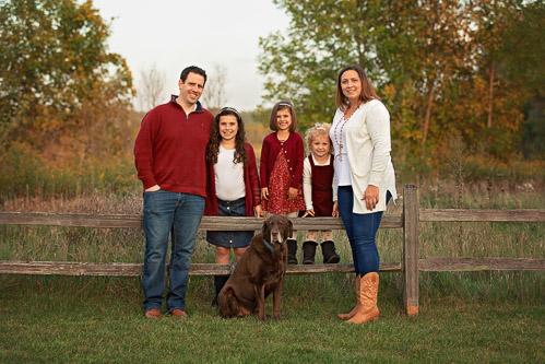 Family of 5 standing along a wooden fence with their dog during a Fall photo session