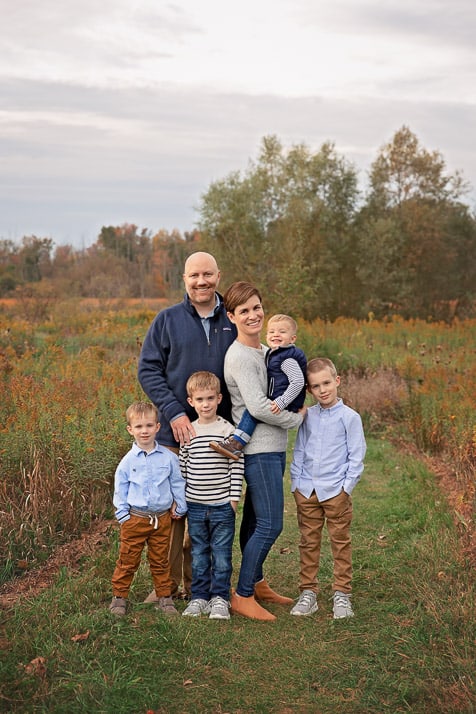 Family of 6 with four young boys standing posed in the middle of a field in Fall