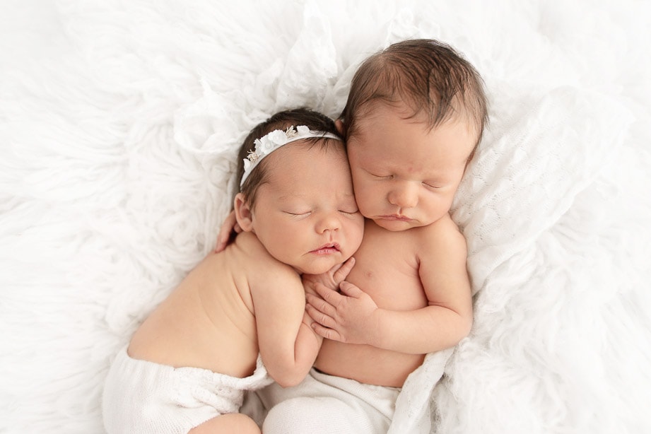 Closeup of newborn girl snuggled on twin brothers chest in a white flokati