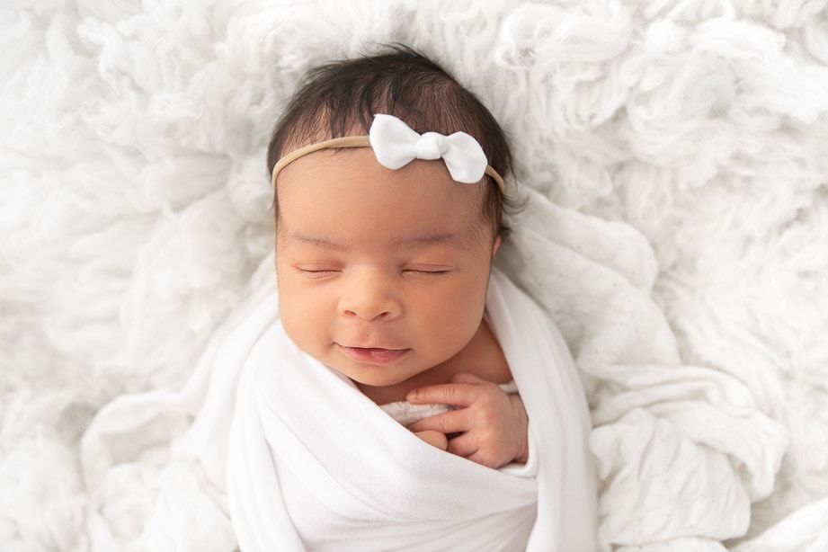 Closeup of Newborn baby girl sleeping on white fur wearing a white bow