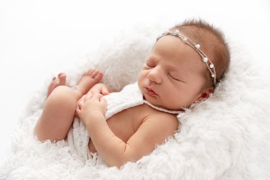 newborn baby girl backlit while sleeping curled up on white fur