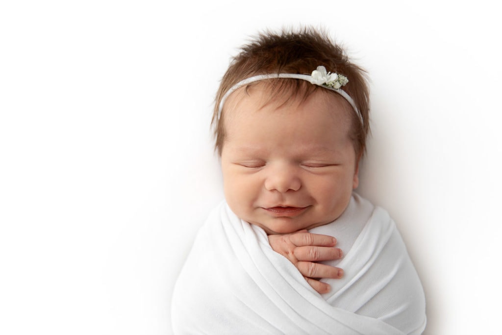 closeup of newborn girl smiling while sleeping wrapped in white fabric