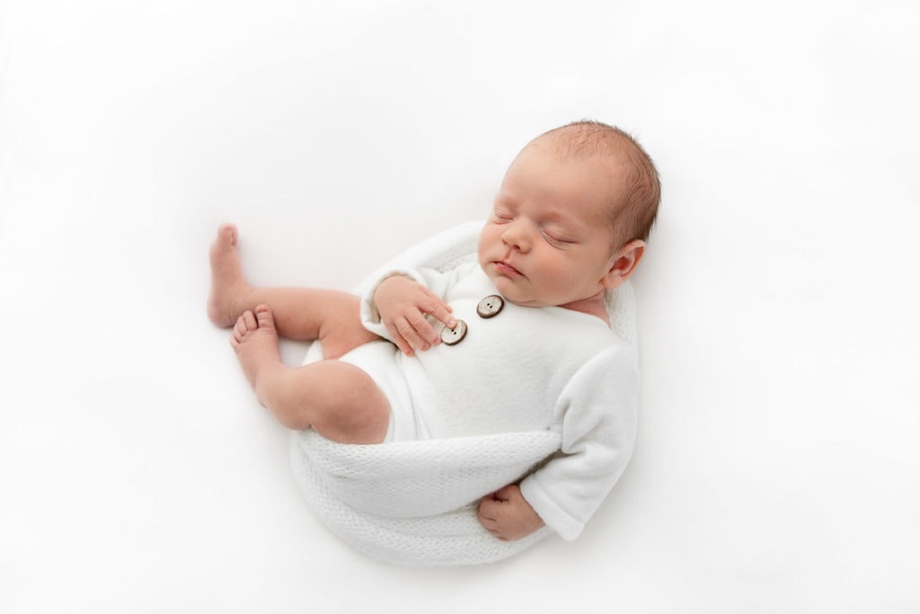 birdseye image of baby boy wearing white romper sleeping on white fabric
