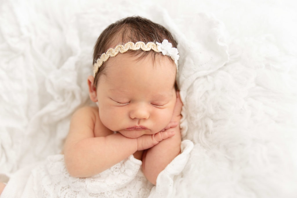 newborn baby girl laying on side with hands under cheek on white flokati