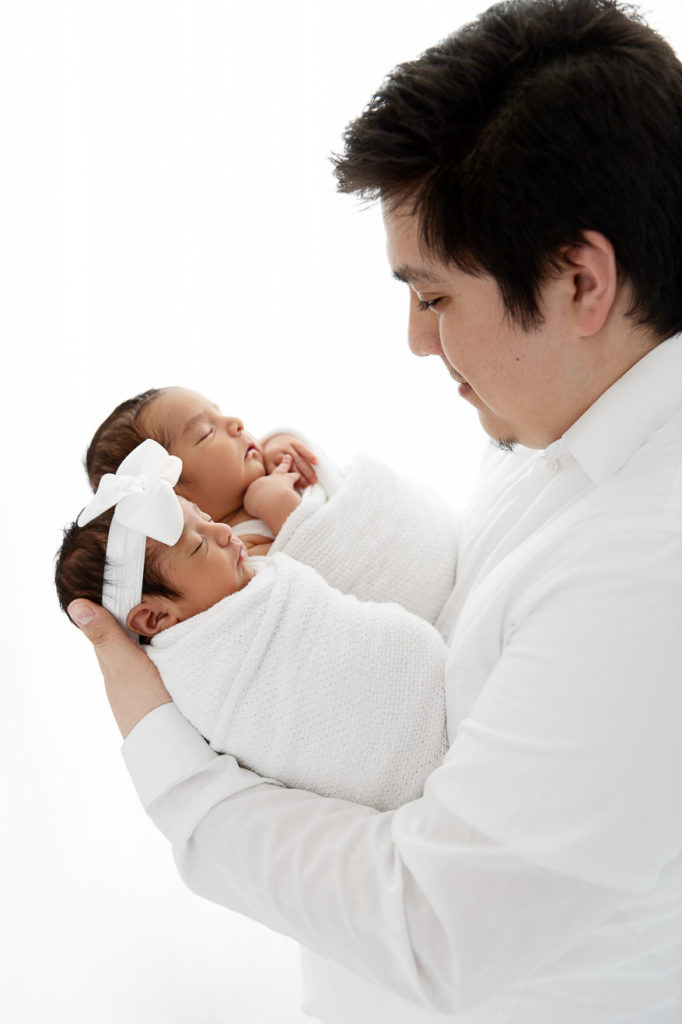 Backlit profile pose of dad holding newborn boy girl twins