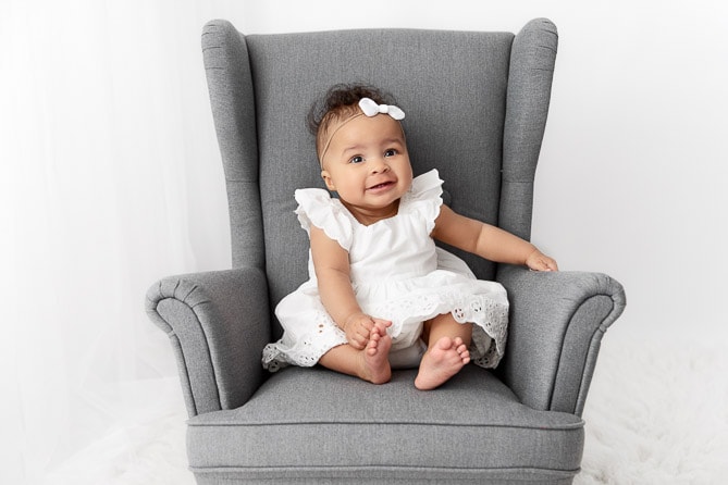 6 month baby girl sitting in a child size gray wingback chair