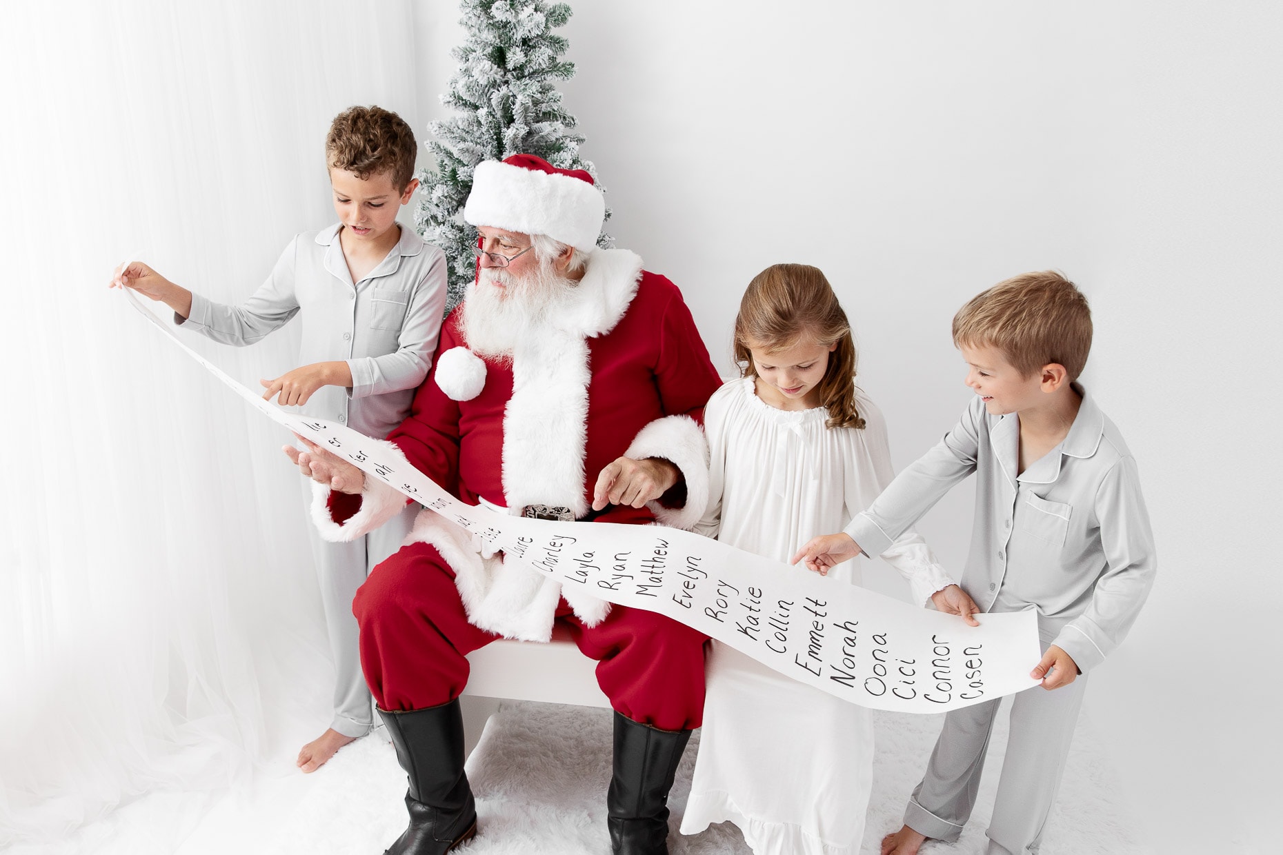 Three young kids looking at a long nice list with Santa Claus in a white studio