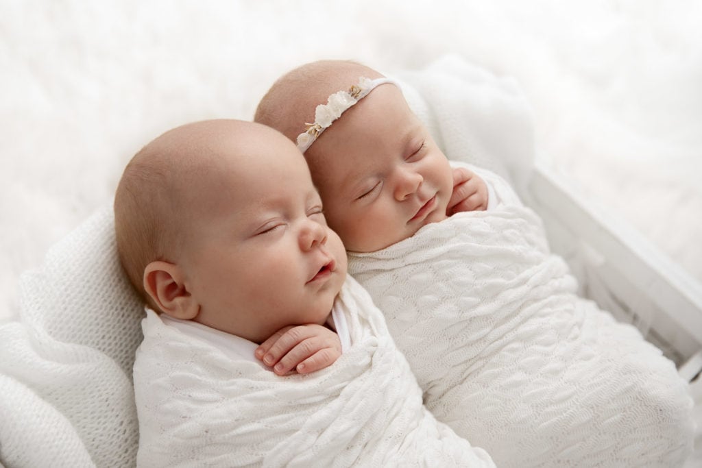 Newborn boy girl twins swaddled sleeping together in a white crate