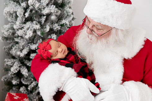 Closeup of Santa holding a newborn baby girl wearing plaid holiday pajamas