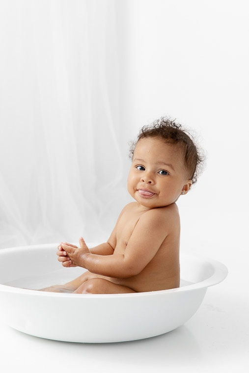 one year old baby girl sitting in a white round bath bowl after her cake smash photo session