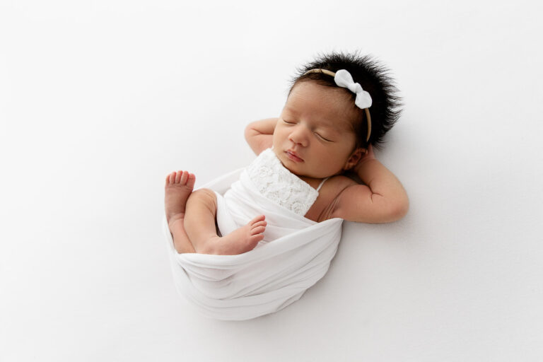 newborn baby girl laying on white beanbag with legs crossed and arms behind head.