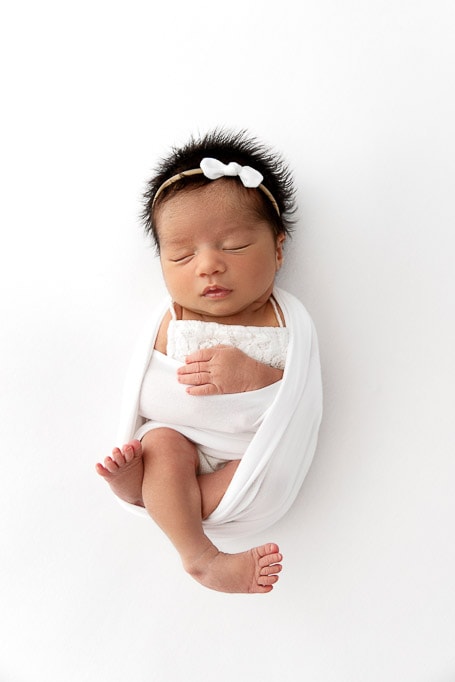 newborn baby girl sleeping while swaddled on a white beanbag