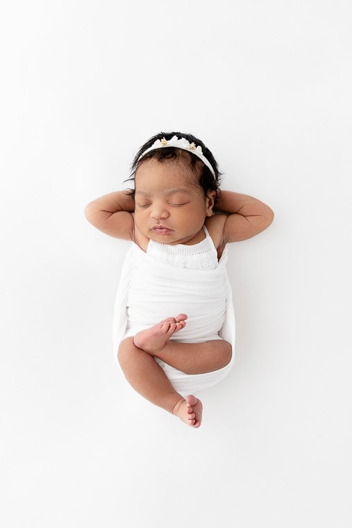 birdseye view of newborn baby girl sleeping on white beanbag with legs crossed and hands behind head