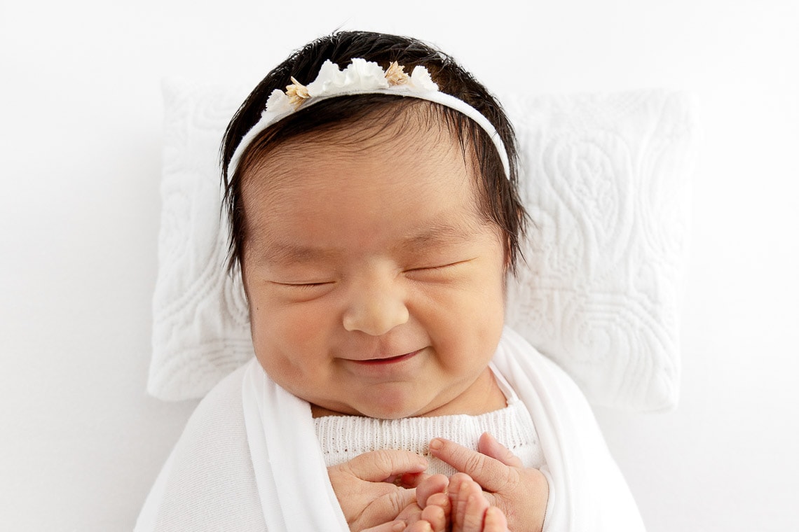 newborn baby girl smiling while sleeping swaddled on a white pillow