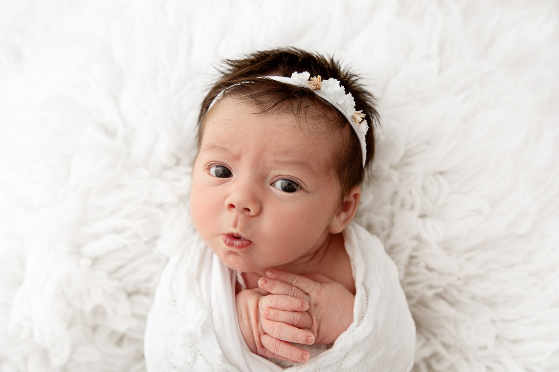 newborn baby girl staring up at camera with puckered lips on a white flokati fur