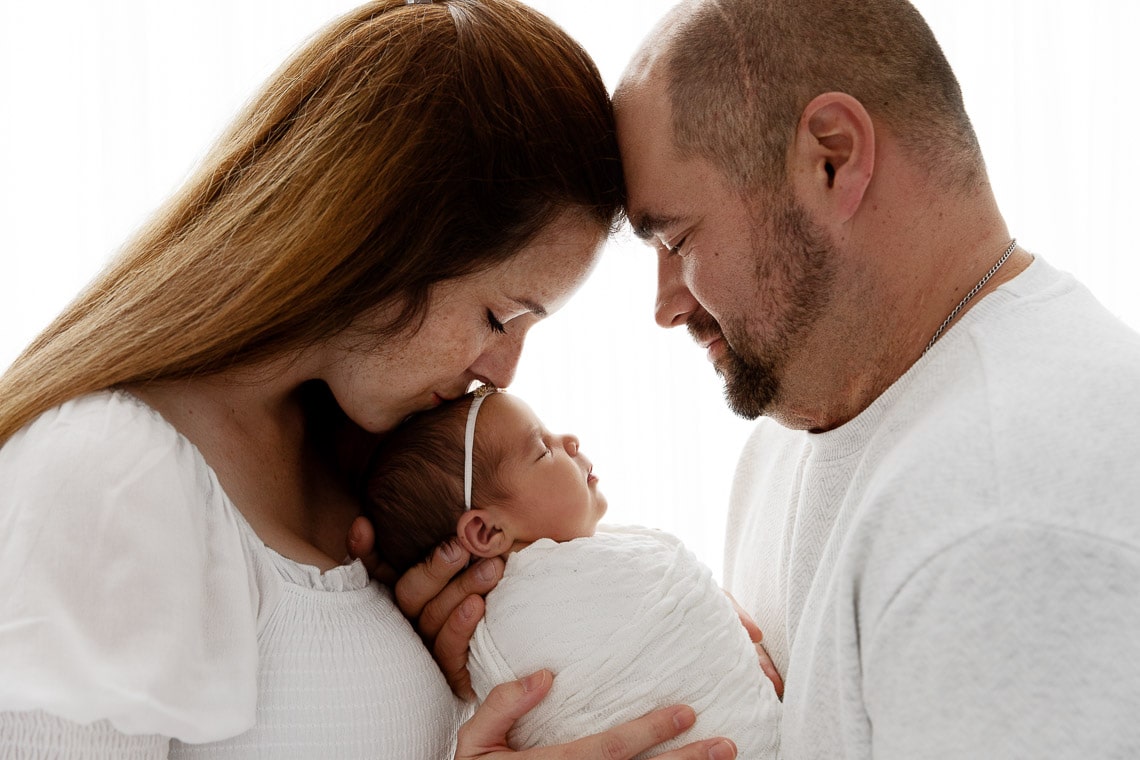 Backlit image of parents holding newborn baby girl while touching foreheads