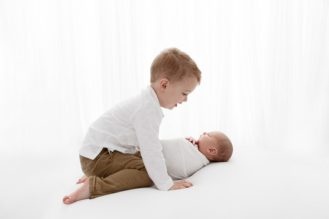 Backlit image of toddler big brother staring down at sleeping newborn brother