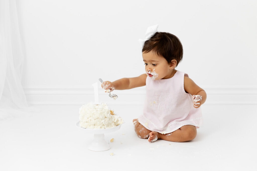 1 year old baby girl digging into a cake with a spoon during her cake smash session
