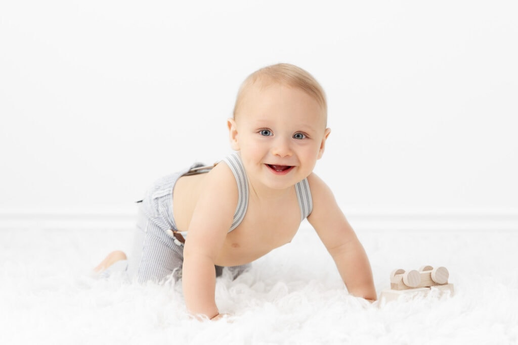 9 month old baby boy in a crawling position wearing light blue and white striped overalls on a white fur rug