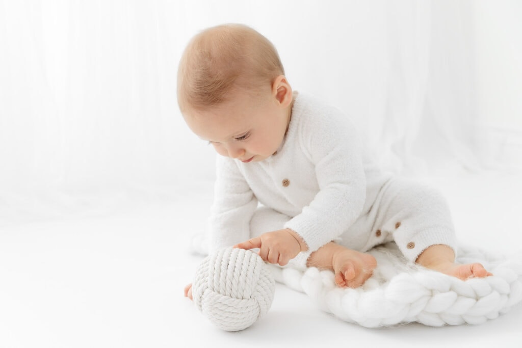 9 month baby boy wearing long fuzzy romper playing with a white knit ball