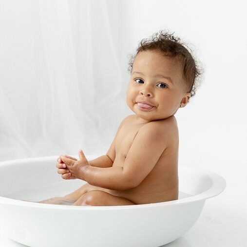 one year old baby girl sitting in a white round bath bowl after her cake smash photo session