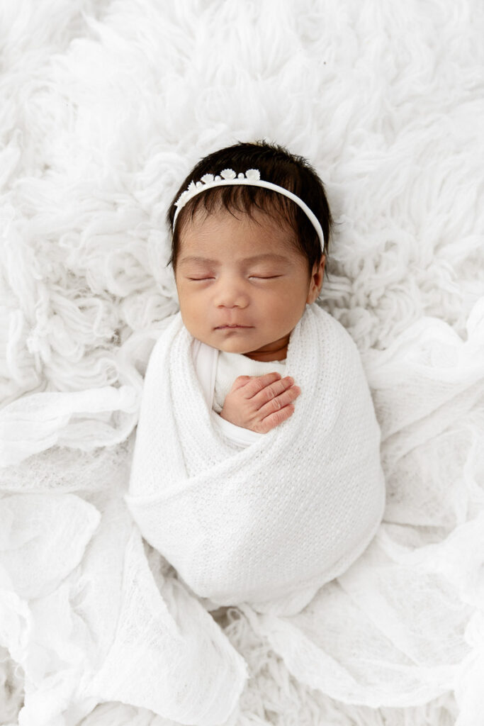 newborn baby girl sleeping swaddled on a white flokati fur