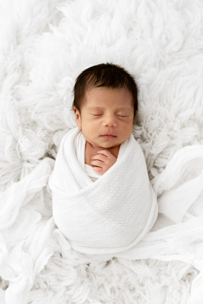 Newborn baby boy sleeping swaddled on a white flokati fur